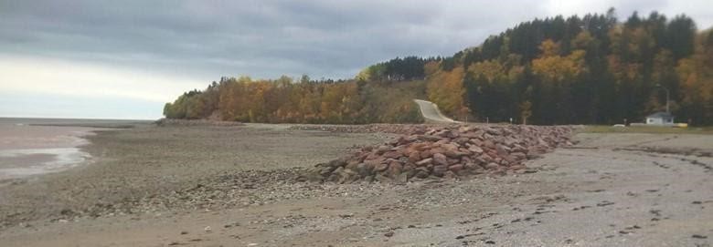 Photographie d’une route longeant une plage rocheuse au Nouveau-Brunswick. Des revêtements rocheux sont placés entre le rivage et la route.
