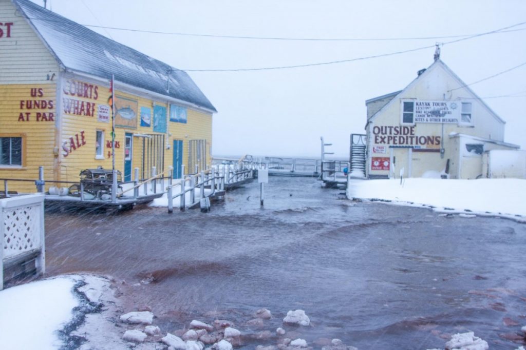 Photograph of two buildings located on the seaside during a winter storm surge event. The area is flooded and wavy.