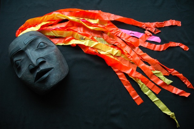A grey mask with red, yellow and pink strands of tape to represent the hair. 